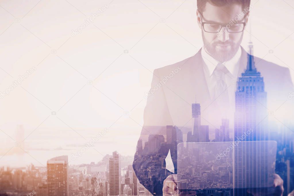 Thoughtful young businessman using laptop on creative New York city background. Communication concept. Double exposure