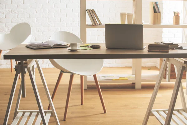 Hipster interior de la oficina con dispositivo, suministros y taza de café en la mesa — Foto de Stock