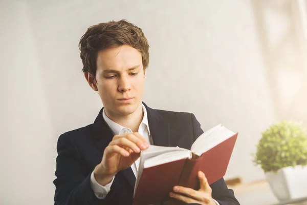 Gros plan portrait d'un jeune homme d'affaires attrayant lisant un livre sur le lieu de travail avec une plante décorative. Fond clair. Concept de connaissance — Photo