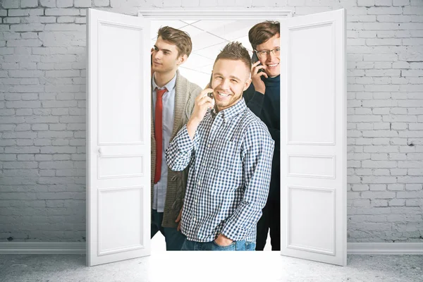 Attractive cheerful european team members talking on the phone behind white doors of brick interior. Communiction concept — Stock Photo, Image
