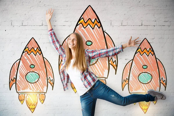 Attractive caucasian girl celebrating success on white brick background with drawn rockets. Entrepreneurship concept — Stock Photo, Image