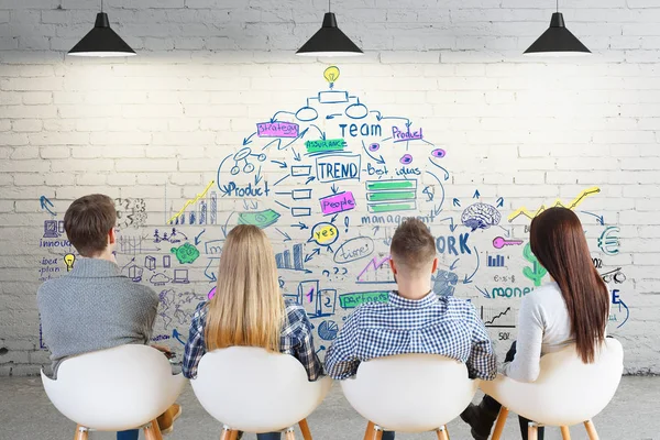 Vista posteriore del giovane team europeo in interni guardando muro di mattoni con schizzo aziendale. Concetto di lavoro di squadra — Foto Stock