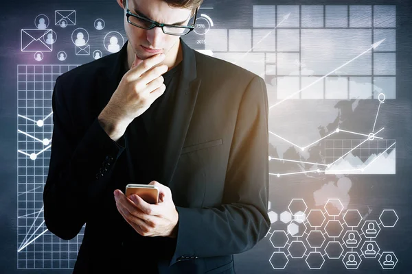 Retrato de pensativo jovem empresário usando smartphone em fundo cinza abstrato com gráficos de negócios digitais. Conceito de comunicação — Fotografia de Stock