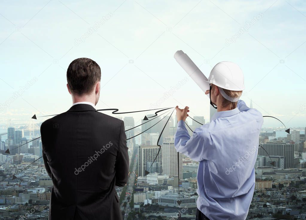 Back view of insdustrial worker explaining something to businessman on city background.  Engineer concept