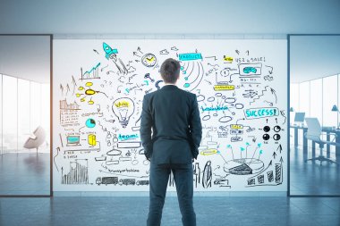 Arkadan görünüşü genç işadamı çalışma alanı ve şehir manzaralı modern iç renkli iş kroki bakarak. Çözüm kavramı. 