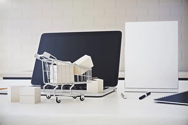 Primo piano del desktop dell'ufficio con schermo del computer portatile vuoto, poster in bianco e piccolo carrello della spesa. Concetto al dettaglio . — Foto Stock