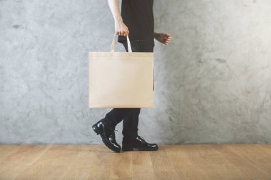 Adamın bacakları ve boş alışveriş çantası elinde beton duvar ve ahşap zemin ile odada yan görünüm. Reklam kavramı. 