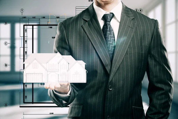 Бізнесмен тримає абстрактну модель будинку в розмитому інтер'єрі. Концепція інженера . — стокове фото