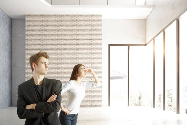 Joven hombre de negocios y mujer mirando a la distancia en el interior de ladrillo con vista a la ciudad y la luz del sol. Concepto de investigación . —  Fotos de Stock