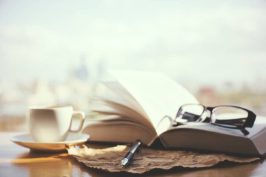 Pencere açık kitap, kahve fincanı, gözlük ve kağıt levha ile. Bulanık şehir arka plan güneş ışığı ile. Yaşam tarzı kavramı