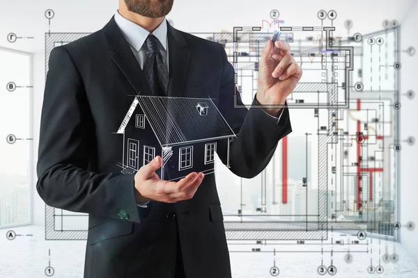 Affärsman holding abstrakt husmodell och ritning på suddiga interiör bakgrund. Tekniska begrepp. — Stockfoto