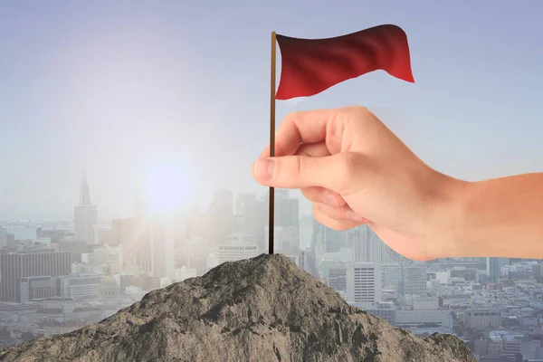 Hand plaatsen van wapperende rode vlag op de bergtop. Achtergrond van de stad. Prestatie concept — Stockfoto