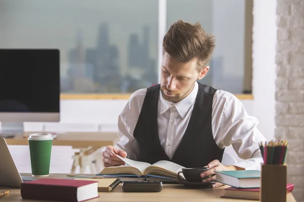 Retrato de un joven hombre de negocios guapo leyendo un libro en un moderno lugar de trabajo de oficina. Concepto de conocimiento — Foto de Stock