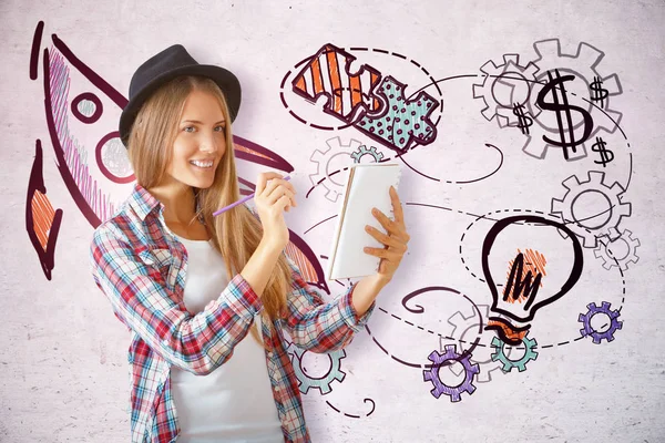 Cheerful young female artist drawing something in notepad on concrete wall background with creative sketch. Presentation concept — Stock Photo, Image