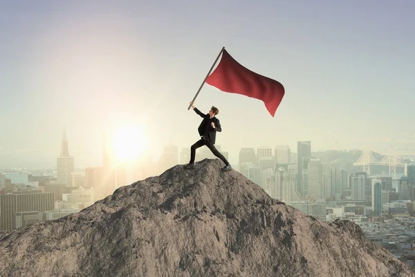 Hombre feliz ondeando bandera roja en la cima de la montaña. Fondo de la ciudad. Concepto de liderazgo —  Fotos de Stock