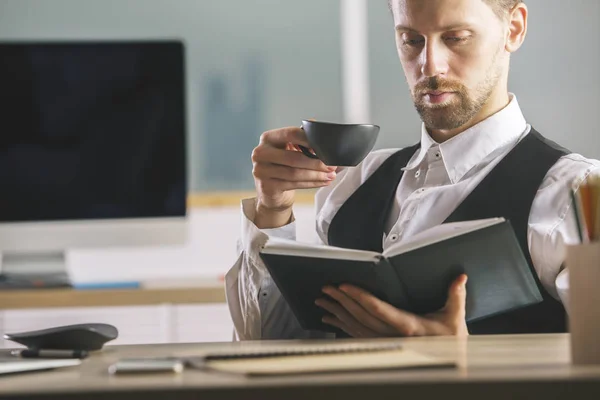 Retrato de un joven hombre de negocios guapo leyendo un libro en un moderno lugar de trabajo de oficina. Concepto educativo — Foto de Stock