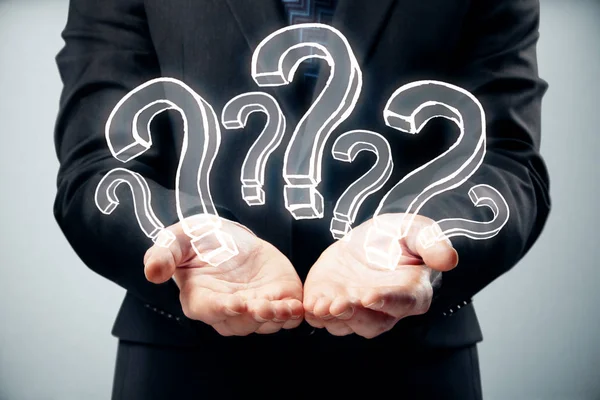 Επιχειρηματίας κρατώντας αφηρημένη συντάσσονται ερωτηματικά σε γκρι φόντο. FAQ έννοια — Φωτογραφία Αρχείου