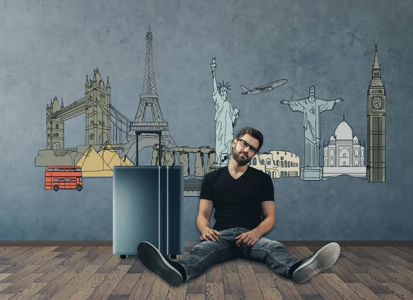 Вид спереди европейского мужчины, сидящего на полу бетонного интерьера комнаты с чемоданом. Концепция путешествия. 3D рендеринг — стоковое фото