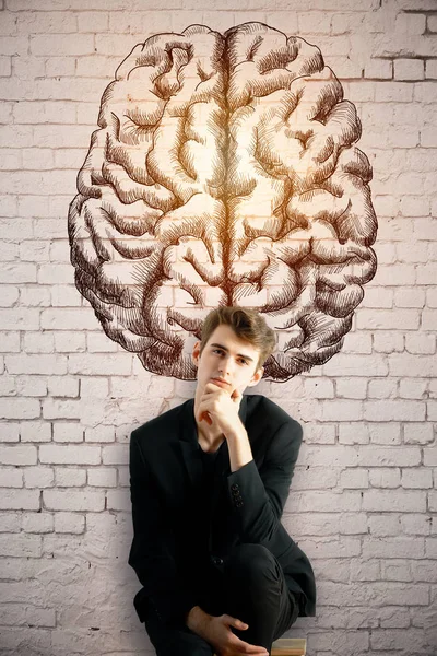 Pensativo joven empresario europeo en el fondo de la pared de ladrillo con dibujo del cerebro creativo. Concepto de tormenta de ideas — Foto de Stock