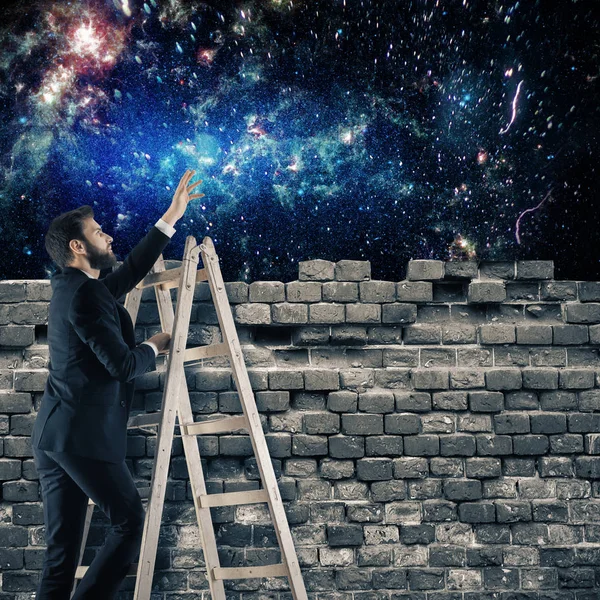 Joven hombre de negocios en escalera mirando el universo desde detrás de la pared de ladrillo. Explorar concepto — Foto de Stock