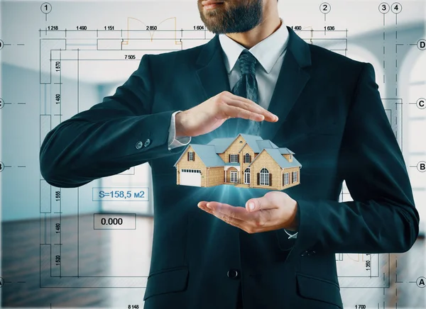 Бизнесмен держит абстрактную модель дома в расплывчатом интерьере с абстрактными проектными чертежами. Концепция архитектуры. 3D рендеринг — стоковое фото