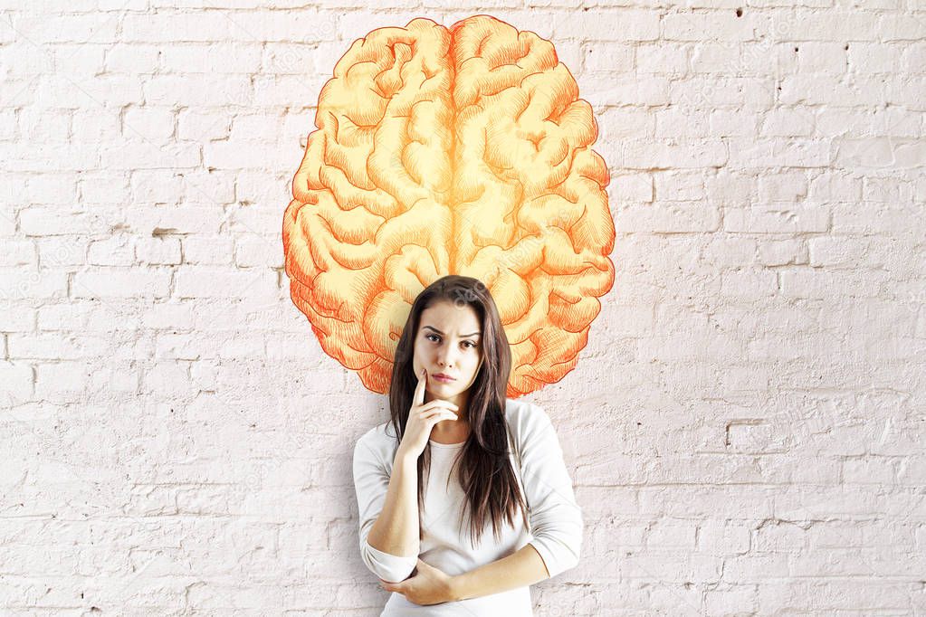 Thoughtful young european businesswoman on brick wall background with creative brain sketch. Intelligence concept