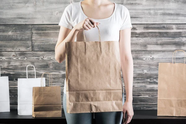 Primer plano de la mujer sosteniendo bolsas de papel artesanales vacías para comprar sobre fondo de pared de hormigón. Concepto para llevar. Prepárate. —  Fotos de Stock