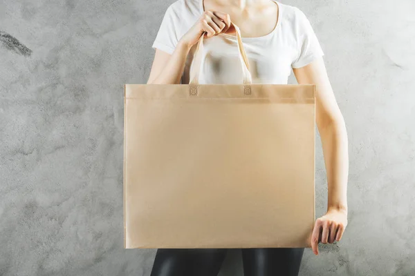 Крупним планом жінка тримає чисту сумку для покупок на фоні бетонних стін. Концепція пакунка. Знущання — стокове фото