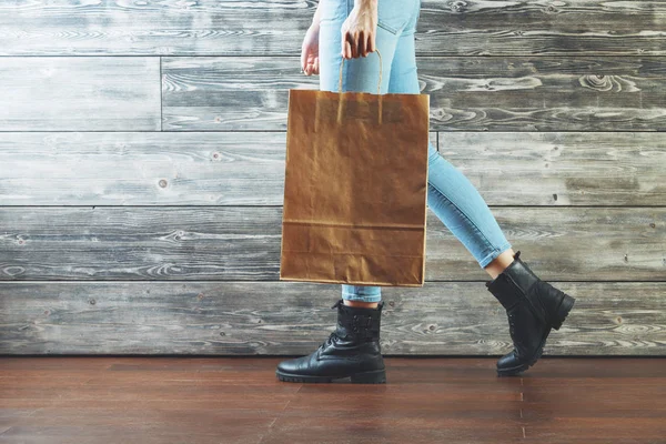 Boş kağıt alışveriş çantası ile kadın bacakları ahşap studio odada yürürken yan görünüm. Tüketim kavramı. Yukarı alay — Stok fotoğraf