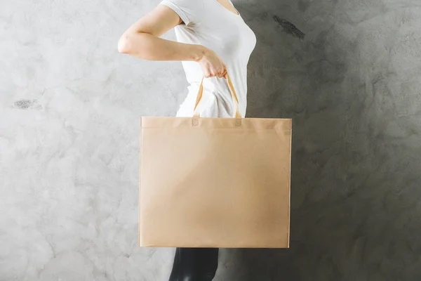 Sidan Visa och närbild på kvinna som håller tom shoppingväska på betongvägg bakgrund. Logotyp-konceptet. Håna upp — Stockfoto