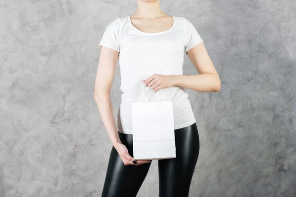 Закрыть женщину с пустым белым бумажным пакетом для покупок на бетонном фоне. Концепция рекламы. Mock up — стоковое фото