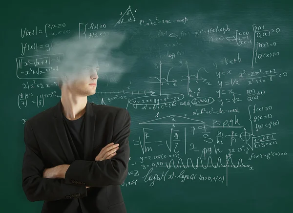 Uomo d'affari dalla testa nuvolosa con le braccia incrociate in piedi su sfondo lavagna con formule matematiche. Concetto di conoscenza — Foto Stock