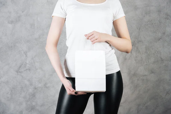 Закрыть женщину с пустым белым бумажным пакетом для покупок на бетонном фоне. Идея супермаркета. Mock up — стоковое фото