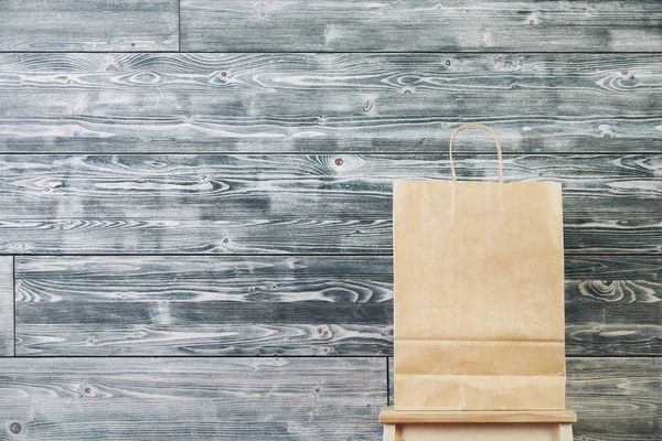 Leere braune Einkaufstasche aus Papier, platziert auf einer Leiter. hölzerne Bretterwand Hintergrund. Einzelhandelskonzept. Attrappe — Stockfoto