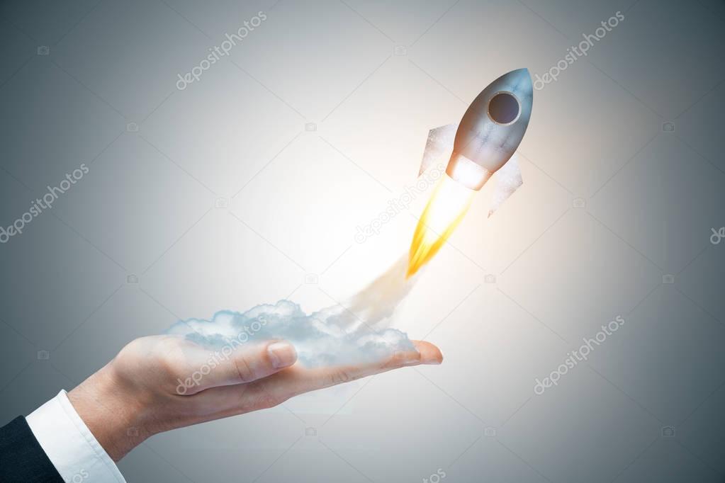 Businessman hand holding abstract launching rocket on gray background. Startup concept. 3D Rendering 