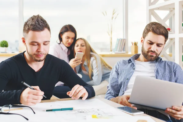 Atractivo grupo europeo joven, hombres y mujeres de negocios que trabajan en el proyecto en la oficina moderna con ordenador portátil, teléfono inteligente, papeleo y otros artículos en el escritorio. Concepto contable —  Fotos de Stock