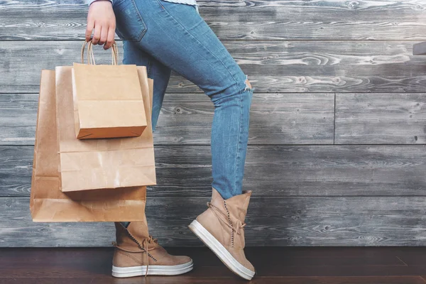 Жінка в стильних кросівках стоїть в кімнаті і тримає порожні сумки для покупок на дерев'яному тлі стін. Концепція купівлі. Знущання — стокове фото