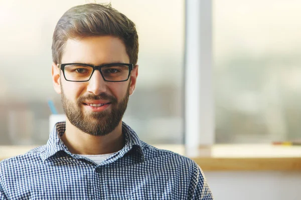 Retrato de atractivo joven hombre de negocios en gafas de pie en la oficina borrosa con vista a la ciudad. Concepto de trabajo —  Fotos de Stock