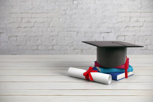 Mortarboard preto, livros e diploma colocado na superfície de madeira e fundo da parede de tijolo. Conceito de educação. Renderização 3D — Fotografia de Stock