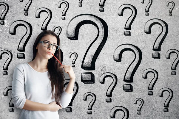 Thoughtful young european woman on brick wall background with drawn question marks. Answer concept — Stock Photo, Image