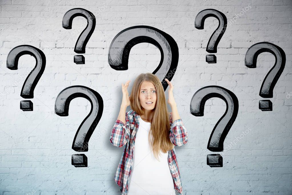 Worried young european woman on brick wall background with drawn question marks. Stress concept 