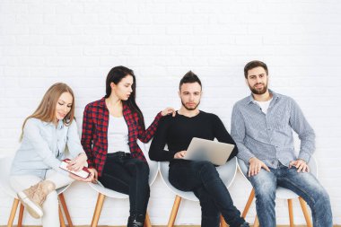 Genç İşadamları ve sandalyelere oturan, kitap okuma ve beyaz Studio dizüstü kullanarak kadın duvar ve ahşap zemin tuğla. Ekip çalışması kavramı 