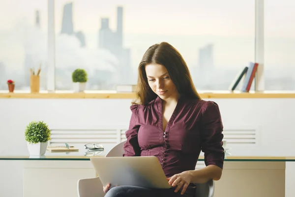 Vacker ung europeisk kvinna använder laptop i kontor med suddiga stadsutsikt. Kommunikationskoncept — Stockfoto