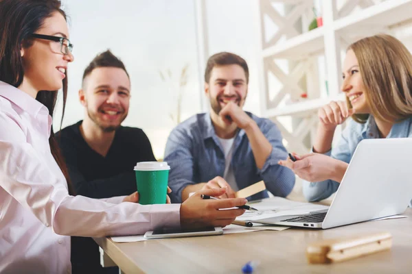 Atractivo grupo europeo joven, hombres y mujeres de negocios que trabajan en el proyecto en la oficina moderna con ordenador portátil, teléfono inteligente, papeleo y otros artículos en el escritorio. Concepto de discusión —  Fotos de Stock