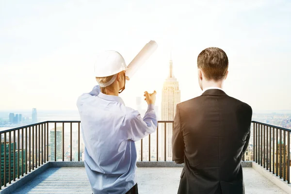 Vista posteriore del giovane uomo d'affari e ingegnere discutere qualcosa sul balcone con vista sulla città. Concetto di lavoro di squadra — Foto Stock