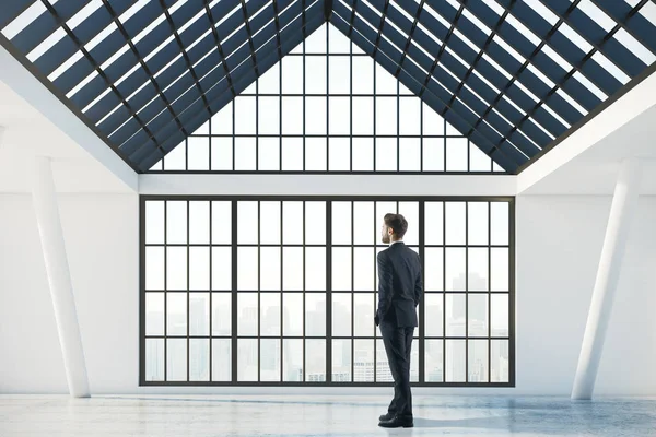 Visão traseira de pensativo jovem empresário em pé no interior concreto abstrato com janelas panorâmicas, vista da cidade e luz solar. Pensa no conceito. Renderização 3D — Fotografia de Stock