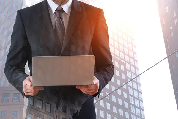 Oigenkännlig affärsman hålla laptop på staden bakgrund. Nätverk-konceptet. Dubbel exponering — Stockfoto