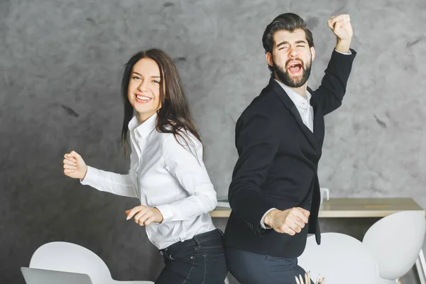 Ritratto di giovani imprenditori attraenti che celebrano il successo in un ufficio moderno. Sfondo murale in cemento. Concetto di successo — Foto Stock