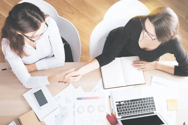 Ansicht von zwei weißen Geschäftsfrauen beim Händeschütteln am Schreibtisch mit Finanzberichten und anderen Artikeln. Partnerschaftskonzept — Stockfoto