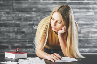 Genç kadın evrak, kitap ve gözlük ile masa üzerinde yaslanmış. Bulanık ahşap duvar arka plan. İş kavramı 